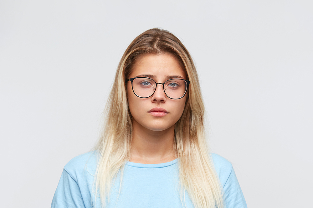 Stock photo of 'Demi' - a young woman in her twenties with long blonde hair and wearing glasses and a pale blue jumper